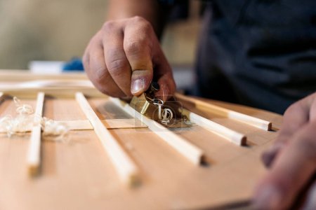 Photo for Unrecognized luthier creating a guitar and using tools in a traditional workshop. - Royalty Free Image