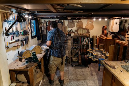 Téléchargez les photos : Luthier méconnu portant un tablier faisant une guitare et travaillant dans son atelier. - en image libre de droit