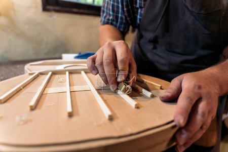 Photo for Unrecognized craftsman creating a guitar and using tools in a traditional workshop. - Royalty Free Image