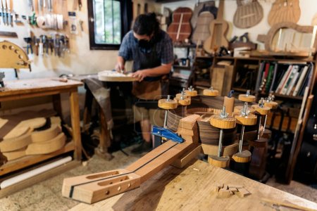 Téléchargez les photos : Luthier portant un masque facial grâce à covid19 faisant une guitare et travaillant dans son atelier. - en image libre de droit