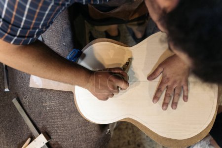 Photo for Unrecognized luthier working in his atelier and making a guitar. He is using a special tools. - Royalty Free Image