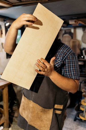 Téléchargez les photos : Luthier non reconnu travaillant dans son atelier et tenant une planche de bois. - en image libre de droit