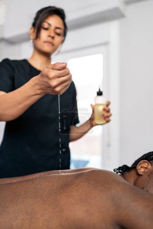 Téléchargez les photos : Adulte femme spa travailleur donnant massage du corps à un client africain et en utilisant de l'huile. - en image libre de droit