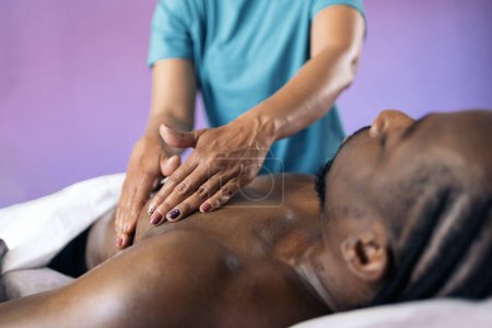 Téléchargez les photos : Femme travailleuse de spa non reconnue qui donne un massage du corps à un bel homme africain. - en image libre de droit