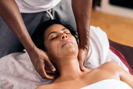 Photo for Relaxed woman lying down and receiving a neck massage. The masseuse is a handsome african american man. - Royalty Free Image