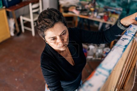 Foto de Pintora femenina concentrada trabajando en lienzo grande con pintura colorida. Tiene un estudio de arte en su garaje.. - Imagen libre de derechos