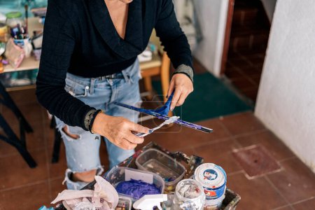 Foto de Pintora femenina no reconocida que mezcla pintura azul y usa equipo en su estudio de arte en casa. - Imagen libre de derechos