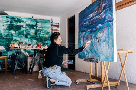 Foto de Pintora enfocada de mediana edad que trabaja en su estudio de arte en casa y usa pintura azul. - Imagen libre de derechos