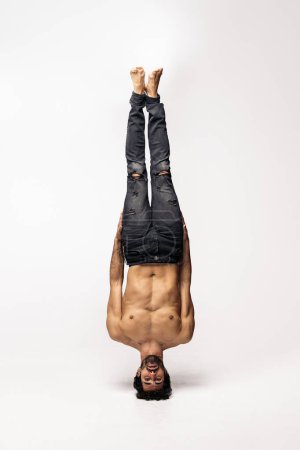 Photo for Expressive male dancer doing headstand in studio shot and looking at camera against white background. He is shirtless. - Royalty Free Image