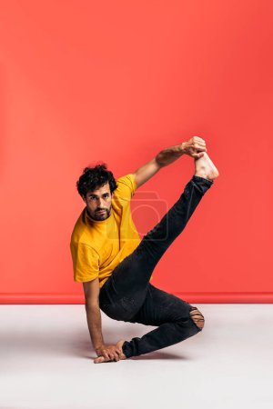 Téléchargez les photos : L'homme expressif s'amuse en studio tourné sur fond rouge dansant et faisant des mouvements de break dance. Il est pieds nus.. - en image libre de droit