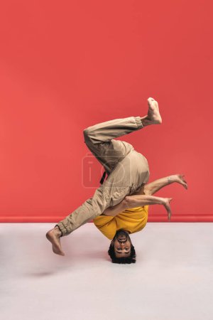 Téléchargez les photos : L'homme expressif s'amuse en studio tourné sur fond rouge dansant et faisant des mouvements de break dance. Il est pieds nus.. - en image libre de droit