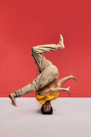 Photo for Expressive man having fun in studio shot against red background dancing and doing break dance moves. He is barefoot. - Royalty Free Image