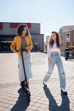 Téléchargez les photos : Gai afro fille équitation scooter électrique avec son ami dans la rue et avoir du plaisir. - en image libre de droit