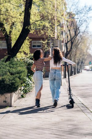 Foto de No reconocido afro niñas montar scooter eléctrico en la calle y divertirse. - Imagen libre de derechos
