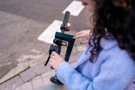 Téléchargez les photos : Jeune femme méconnue aux cheveux bouclés utilisant un scooter électrique dans la rue et s'amusant. - en image libre de droit