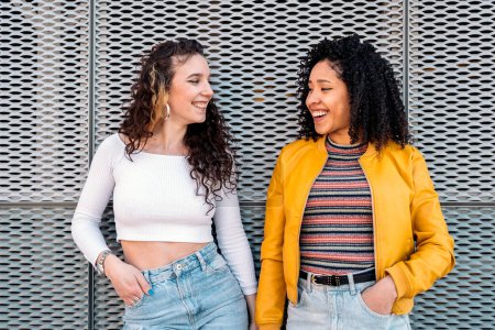 Photo for Beautiful young girls with curly hair smiling and looking at each other outdoors. - Royalty Free Image