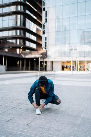 Foto de Joven bailarín no reconocido atando los cordones de sus zapatillas en la calle antes de bailar. - Imagen libre de derechos