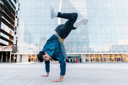 Photo for Talented young man with casual clothes doing break moves in the street against big modern buildings in the city. - Royalty Free Image