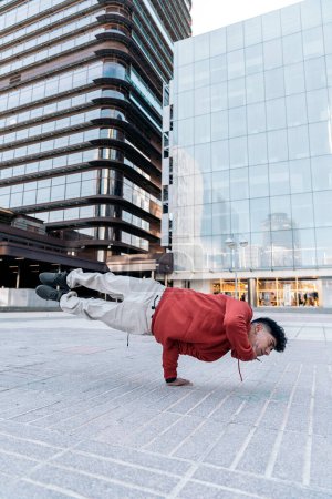 Téléchargez les photos : Garçon talentueux pratiquant le break dance dans la rue contre les grands bâtiments modernes. - en image libre de droit