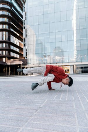 Téléchargez les photos : Garçon talentueux pratiquant le break dance dans la rue contre les grands bâtiments modernes. - en image libre de droit
