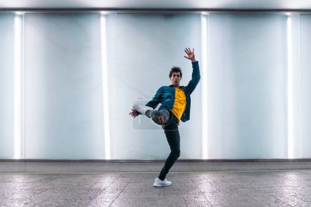 Photo for Talented young man practicing break dance against white wall with lights and looking at camera. - Royalty Free Image