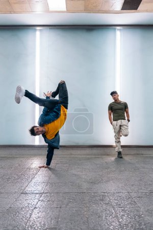 Foto de Dos amigos multiétnicos bailando break dance y divirtiéndose contra la pared blanca con luces. - Imagen libre de derechos