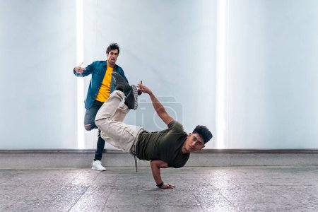 Téléchargez les photos : Incroyables jeunes hommes pratiquant la danse de rupture ensemble contre un mur blanc avec des lumières. - en image libre de droit