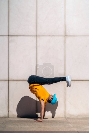 Téléchargez les photos : Un jeune garçon confiant fait des danses de break dance contre un mur blanc dans la rue. - en image libre de droit