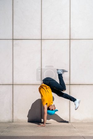 Photo for Cool young man doing break dance dances against white wall in the street. - Royalty Free Image