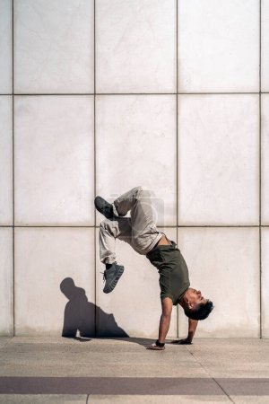 Photo for Cool young hispanic man doing break dance dances against white wall in the street. - Royalty Free Image