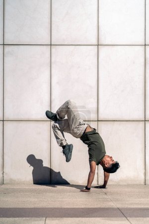 Photo for Confident young boy doing break dance dances against white wall in the street. - Royalty Free Image