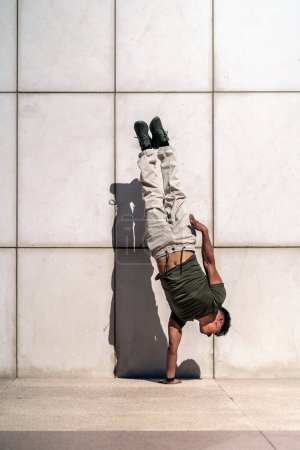 Téléchargez les photos : Un jeune garçon confiant fait des mouvements de break dance contre un mur blanc dans la rue. - en image libre de droit