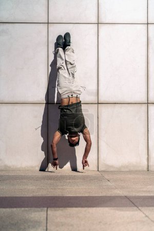 Foto de Guay joven hispano haciendo break dance baila contra pared blanca en la calle. - Imagen libre de derechos