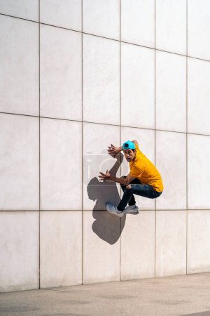 Photo for Confident young man doing break dance dances against white wall in the street. - Royalty Free Image
