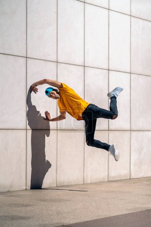 Confident young boy doing break dance dances against white wall in the street.