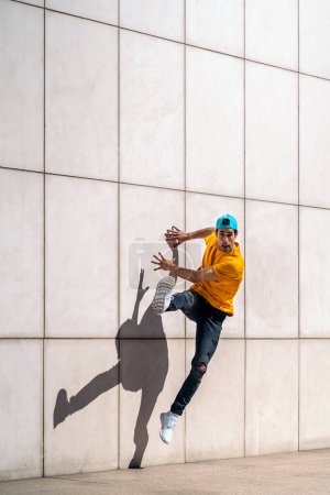 Téléchargez les photos : Un jeune garçon confiant fait des danses de break dance contre un mur blanc dans la rue. - en image libre de droit