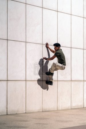 Téléchargez les photos : Cool jeune homme hispanique faire des danses de rupture contre mur blanc dans la rue. - en image libre de droit