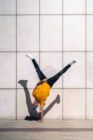 Photo for Confident young boy doing break dance dances against white wall in the street. - Royalty Free Image