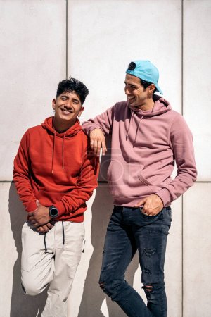 Photo for Happy and cool male friends smiling and looking at camera against white wall. - Royalty Free Image