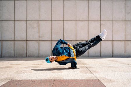 Téléchargez les photos : Talentueux jeune homme faisant des danses de break dance contre un mur blanc dans la rue et regardant la caméra. - en image libre de droit