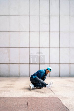Téléchargez les photos : Un jeune homme confiant fait des danses de break dance contre un mur blanc dans la rue. - en image libre de droit