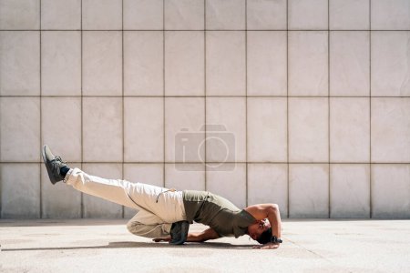 Téléchargez les photos : Garçon hispanique confiant qui danse contre un mur blanc dans la rue. - en image libre de droit
