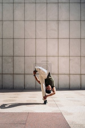 Foto de Confiado chico hispano haciendo break dance contra pared blanca en la calle. - Imagen libre de derechos