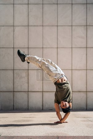 Photo for Cool young latin man doing break dance moves in the street and showing his talent. He is looking at camera. - Royalty Free Image