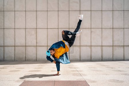 Photo for Talented young man doing break dance dances against white wall in the street and looking at camera. - Royalty Free Image