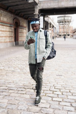Foto de Hombre africano feliz y elegante caminando por la calle y usando su teléfono celular. - Imagen libre de derechos