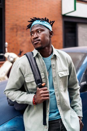 Téléchargez les photos : Jeune et confiant homme africain debout dans la rue et regardant vers le côté. - en image libre de droit