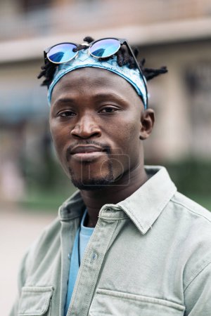 Téléchargez les photos : Jeune garçon afro-américain avec dreadlocks et bandana bleu regardant caméra dans la ville. - en image libre de droit
