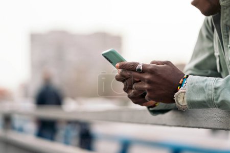 Téléchargez les photos : Jeune homme africain non reconnu debout dans la rue et utilisant son téléphone portable. - en image libre de droit
