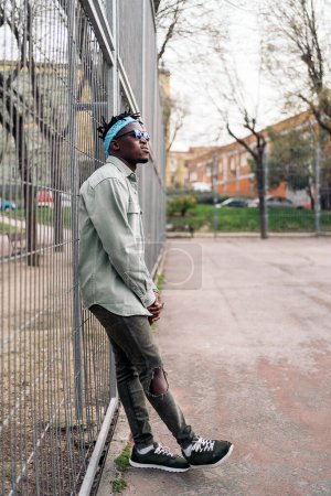 Téléchargez les photos : Jeune et cool homme noir debout dans une clôture et regardant devant. - en image libre de droit